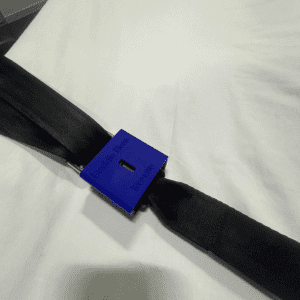 A close-up view of the 'Buckle Boss Rescue' tool, a blue safety device, clasped onto a black seat belt laid on a white background.