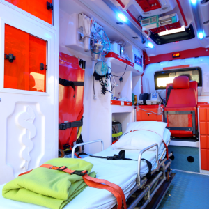 Interior of a modern, well-equipped ambulance featuring a single stretcher with a white sheet and green blanket, various medical supplies, and emergency equipment. 