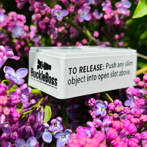 A close-up image of the Buckle Boss Classic, a seatbelt release tool, set against a backdrop of vibrant purple lilac flowers.