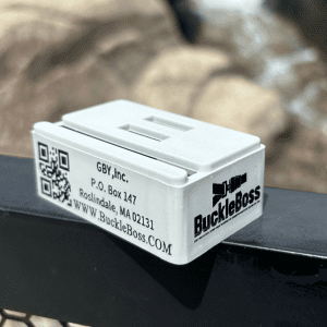 Close-up image of a white plastic product labeled 'BuckleBoss Classic' with a logo. It features a slot on the top resembling a buckle.