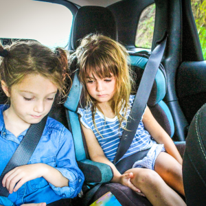 Two young girls, seated in a car's backseat, display contrasting emotions during a car ride. 